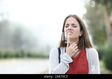 Vista frontale ritratto di una donna malata sofferenza mal di gola passeggiate in un parco di un nebbioso giorno Foto Stock