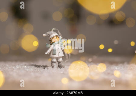 Decorazione di Natale figurine a tema. Statuetta boy in maglia cappelli e sciarpe. Decorazione per albero di Natale. Decorazioni festive, calde luci bokeh di fondo Foto Stock