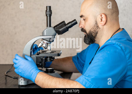 Maschio assistente di laboratorio esaminando campioni di biomateriale in un microscopio Foto Stock
