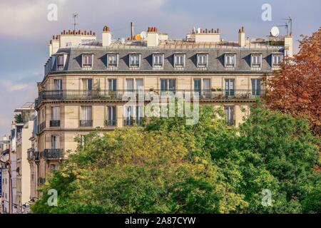 Un Parigino tradizionale edificio di appartamenti in un quartiere residenziale, con alberi di grandi dimensioni aggiungendo la natura per il contesto urbano. Foto Stock