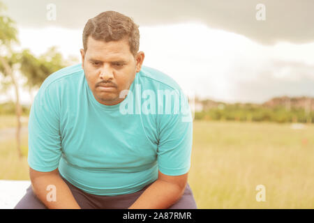Seriamente fat man su all'aperto, parco - Concetto di tristezza a causa del sovrappeso - Indiano obesi sensazione uomo infelice o premuto. Foto Stock