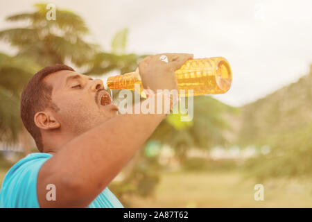 Fat giovane uomo acqua potabile dalla bottiglia outdoor - Sete obeso di acqua potabile dopo esercizio. Foto Stock