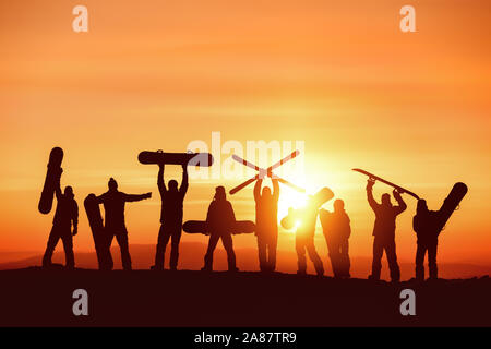 Grande gruppo di sagome di felice di sciatori e snowboarder si divertono contro il cielo al tramonto. Ski resort concept Foto Stock