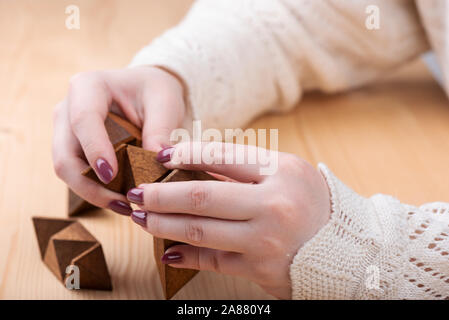 Una ragazza sta cercando di assemblare una stella dodecaedro puzzle. Dodici facciate piccola a forma di stella dodecaedro al di sopra di un tavolo di legno. Concetto di puzzle. Foto Stock