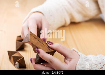 Una ragazza sta cercando di assemblare una stella dodecaedro puzzle. Dodici facciate piccola a forma di stella dodecaedro al di sopra di un tavolo di legno. Concetto di puzzle. Foto Stock