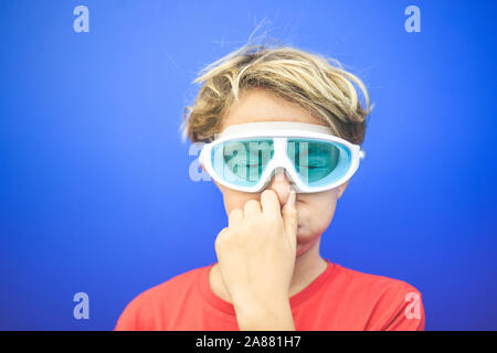 Bel ragazzo con gli occhi strizzati naso chiuso indossando maschera subacquea, isolata su uno sfondo blu. Immagine colorata di un giovane maschio divertendosi con scuba Foto Stock