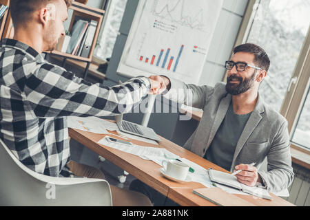 Startupers maschio lavorando insieme a Office seduta agitando mani cordiale messaggio di saluto Foto Stock