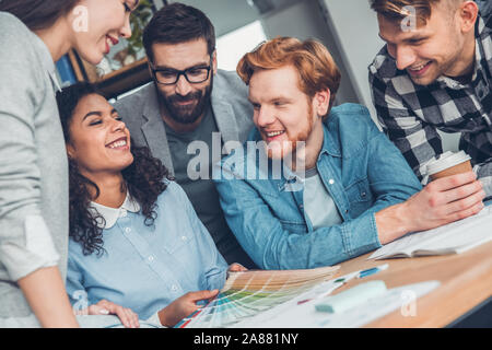 Startupers lavorando insieme a Office seduta palette di trattenimento di ridere close-up Foto Stock