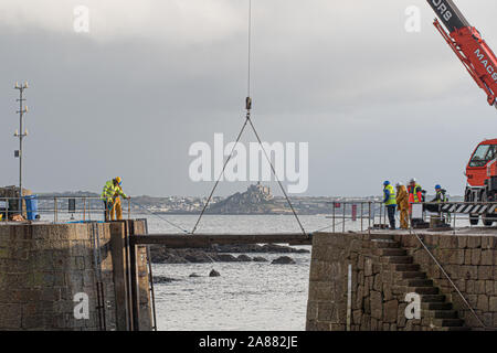 Mousehole, Cornwall, Regno Unito, 7 novembre 2019. Regno Unito Meteo. Ogni anno giant degli spessori di legno vengono abbassati delicatamente nell'apertura di Mousehole Harbour, per proteggerlo dalle tempeste invernali. Visto in background St Michaels Mount a Marazion. Simon credito Maycock / Alamy Live News. Foto Stock