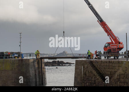 Mousehole, Cornwall, Regno Unito, 7 novembre 2019. Regno Unito Meteo. Ogni anno giant degli spessori di legno vengono abbassati delicatamente nell'apertura di Mousehole Harbour, per proteggerlo dalle tempeste invernali. Visto in background St Michaels Mount a Marazion. Simon credito Maycock / Alamy Live News. Foto Stock