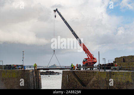 Mousehole, Cornwall, Regno Unito, 7 novembre 2019. Regno Unito Meteo. Ogni anno giant degli spessori di legno vengono abbassati delicatamente nell'apertura di Mousehole Harbour, per proteggerlo dalle tempeste invernali. Visto in background St Michaels Mount a Marazion. Simon credito Maycock / Alamy Live News. Foto Stock