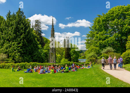 Un gruppo di bambini della scuola di mangiare il pranzo di fronte alla ex Bristol alta croce di giardini Stourhead, Wiltshire, Inghilterra, Regno Unito Foto Stock