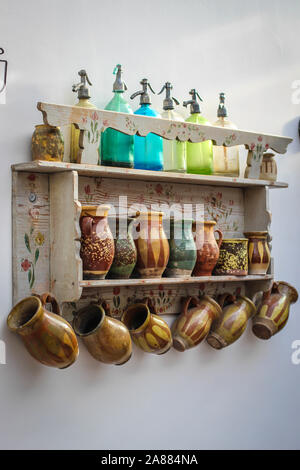 Ripiano decorativo con antichi sifone soda bottiglie e tazze di ceramica sulla parete in cucina in Serbia Foto Stock