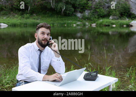 Bel giovane uomo che parla al telefono e utilizzando il computer mentre si lavora. Freelance lavoro distanti, usando un computer portatile Foto Stock