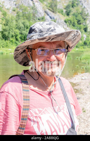 Ritratto di un intelligente uomo anziano con gli occhiali. barbuto annoso vecchio in un cappello sorrisi contro lo sfondo di parcheggiare all'esterno. La mezza età se Foto Stock