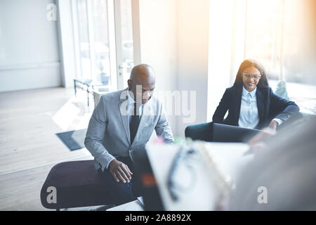 Due africani imprenditori americani sorridere mentre avente una riunione con i colleghi in un luminoso ufficio moderno Foto Stock