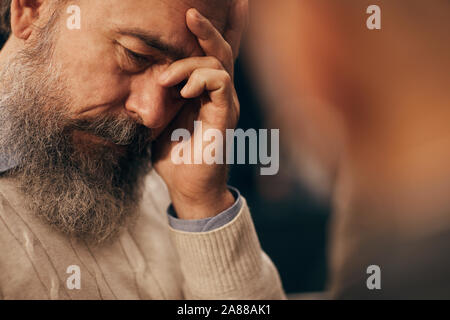 L'uomo anziano con la barba guardando molto triste egli seduto e dicendo circa i suoi problemi per la donna Foto Stock