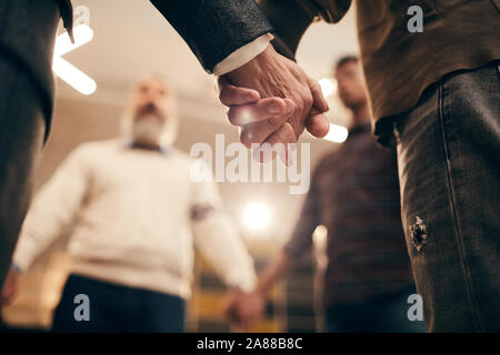 Close-up di persone in piedi e tenendo le mani durante la formazione aziendale in ufficio Foto Stock