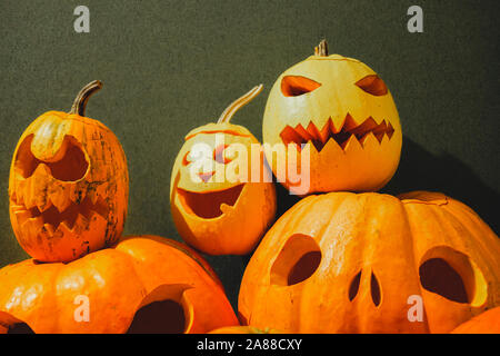 Scolpite zucche di Halloween su sfondo verde. Concetto di Halloween: pila di Jack o'lanterna zucche con facce spaventoso Foto Stock