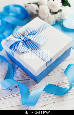 Confezione regalo con prua. Nastri e buste postali in raso blu. Fiori sullo sfondo. Foto Stock