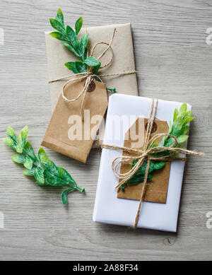 Composizione con scatole da regalo in stile naturale, elementi decorativi floreali e arco rustico a spago su sfondo in legno. Foto Stock