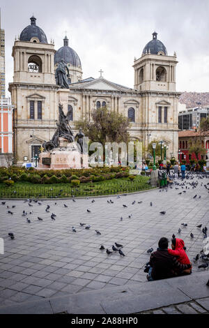 Giovane seduto su Plaza Murillo nel centro storico con la Cattedrale di Nostra Signora della Pace in background, La Paz, Bolivia Foto Stock