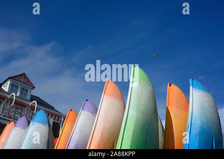 Concetto astratto vista laterale di coloratissimi kayak impilati insieme contro un cielo blu sulla costa del Regno Unito. Un sacco di spazio per il testo. Foto Stock