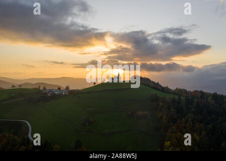Vista aerea delle colline, colorato e la foresta Sv Sobota chiesa. Slovenia il tramonto in autunno Foto Stock