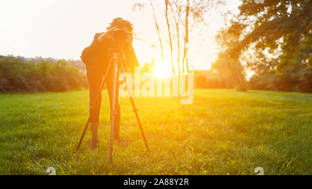 Fotografo di natura con la fotocamera sul cavalletto mentre si fotografa in una campagna al tramonto Foto Stock