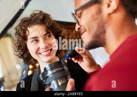 Fotografo con la pulizia della lente con soffietto nella foto studio accanto a un assistente Foto Stock