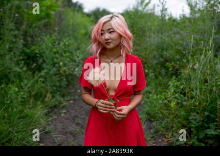 Giovane donna che indossa un abito rosso che tiene testa di seme Foto Stock
