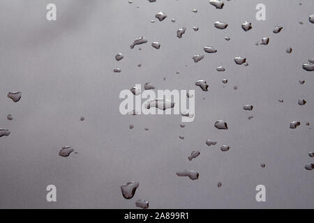 Le gocce di pioggia e il cielo di riflessione su un grigio cofano auto. Gocce di acqua dopo la pioggia su metallo verniciato. Abstract texture di sfondo. Foto Stock