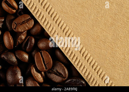 Extreme close up di texture di caffè tostato in grani e caffè filtro a cono da filati greggi, carta riciclata. Macro sfondo alimentare, ospitale nei confronti dei eco Foto Stock