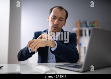 Primo piano del giovane imprenditore tenendo il polso doloroso con la tastiera sulla scrivania in ufficio Foto Stock