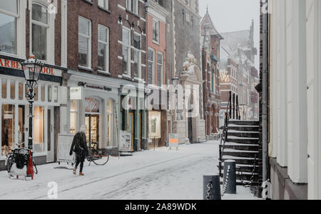 Una ragazza solitaria passeggiate lungo i negozi in un vuoto di coperta di neve Oudestraat a Kampen, Paesi Bassi Foto Stock