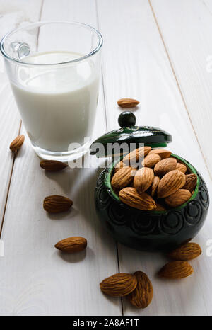 Mandorle e un bicchiere di latte di mandorla su un bianco tavolo in legno Foto Stock