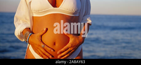 Metà vista in sezione di una donna incinta toccando il suo addome, Oak Street Beach, Chicago, Illinois, Stati Uniti d'America Foto Stock