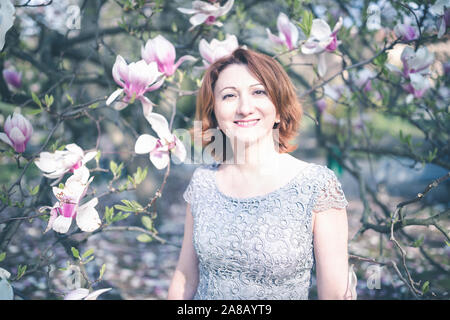 Allegro di mezza età donna armena in un elegante abito sotto la magnolia albero in fiore. Foto Stock