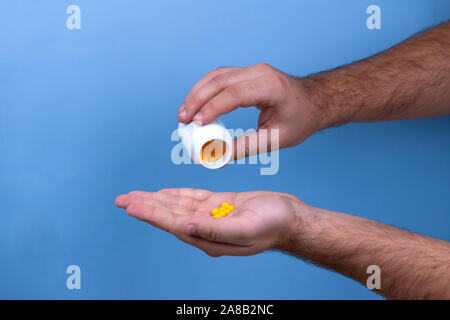 Man mano trattiene il giallo farmaco capsule di omega 3, riversa da una bottiglia bianca in Palm l'olio di pesce, supplemento sano pillole Foto Stock