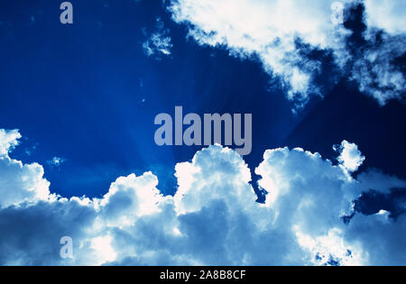 Raggi di sole splendente da dietro il bianco delle nuvole in cielo blu Foto Stock