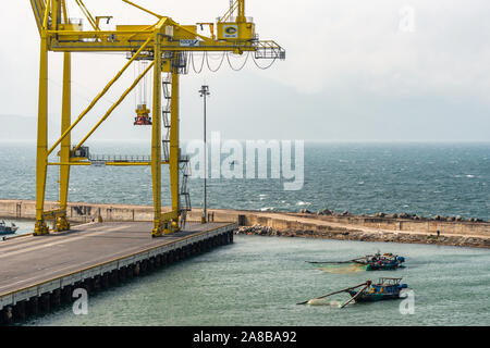 Da Nang, Vietnam - Marzo 10, 2019: Tien Sa Porto di Da Nang Bay. 2 piccole imbarcazioni da pesca si avvicinano al dock con minimo contenitore giallo gru. Banco di nebbia Foto Stock