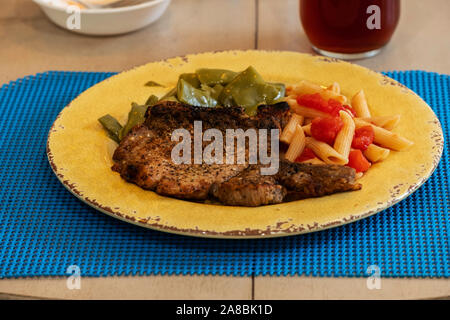 Un braciole di maiale alla griglia cena con penne pasta e pomodori, Italiano fagioli verdi su una piastra di colore giallo. Stati Uniti d'America. Foto Stock