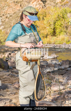 Una donna che prepara la sua canna da pesca con la linea e un gancio come ella capi sulla Poudre fiume per un pomeriggio di pesca. Foto Stock