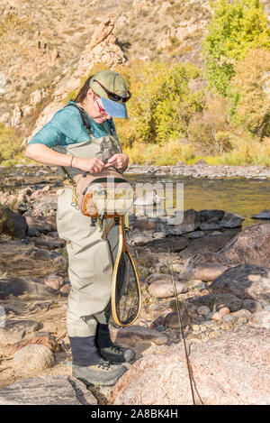 Una donna che prepara la sua canna da pesca con la linea e un gancio come ella capi sulla Poudre fiume per un pomeriggio di pesca. Foto Stock