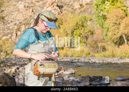 Una donna che prepara la sua canna da pesca con la linea e un gancio come ella capi sulla Poudre fiume per un pomeriggio di pesca. Foto Stock