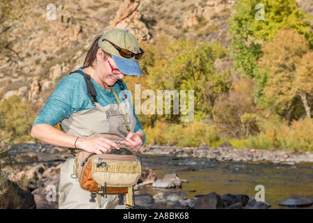 Una donna che prepara la sua canna da pesca con la linea e un gancio come ella capi sulla Poudre fiume per un pomeriggio di pesca. Foto Stock