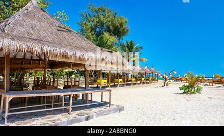 Idilliaca isola tropicale. Una bella sabbia bianca spiaggia pubblica con rustici, con tetto in paglia capanne sulla spiaggia per i turisti su l'isola di Gili Air, Indonesia. Foto Stock