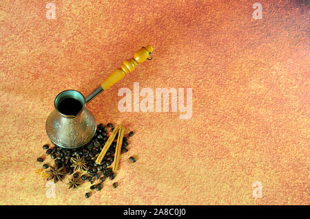 Turk con caffè appena fatto in un mucchio di chicchi di caffè con bastoncini di cannella e anice, su un marrone sfondo astratto. Close-up. Foto Stock