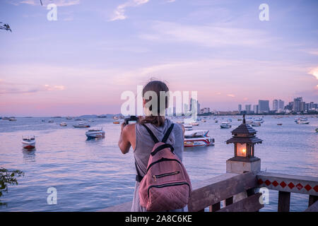 Pattaya, Tailandia - 19 Aprile 2019: bella donna prendendo una foto del tramonto. Felice giovane donna con una macchina fotografica e uno zaino. Foto Stock