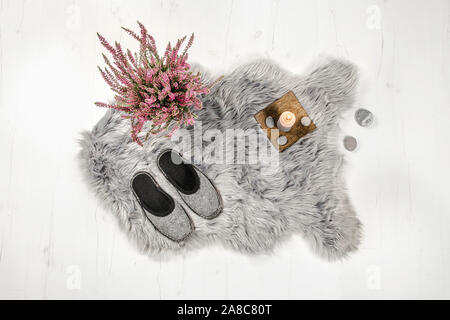 Appartamento vista laici di grigio caldo e accogliente complesso decorativo di pelle di pecora falsa forma tappeto in legno bianco pavimento della scheda con naturale pantofole in feltro e heather flowe Foto Stock